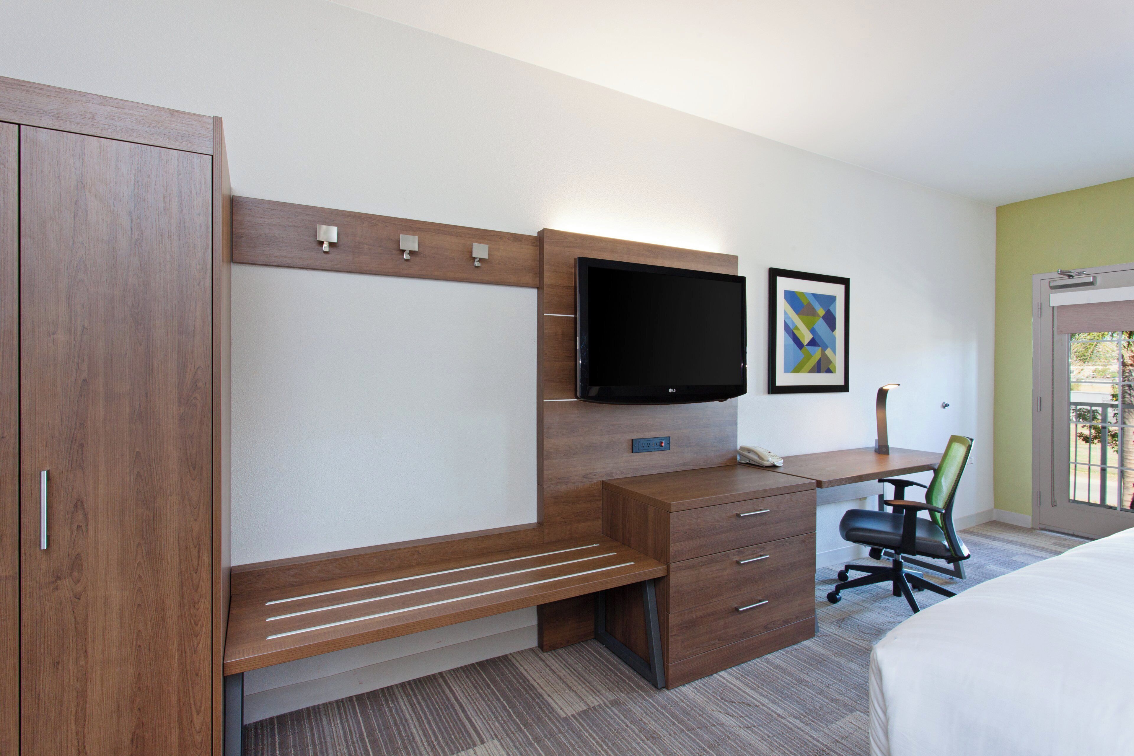 A hotel room with a wooden desk, a flat-screen TV, a bed, and a window with a view.