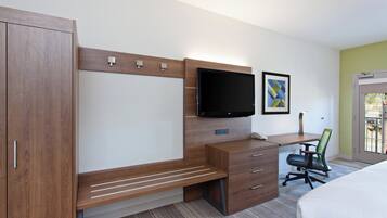 A hotel room with a wooden desk, a flat-screen TV, a bed, and a window with a view.