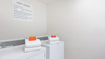 A hotel laundry area with two white front-loading washing machines and a sign with laundry instructions.