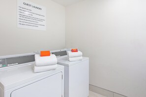 A hotel laundry area with two white front-loading washing machines and a sign with laundry instructions. - Holiday Inn Express & Suites Corona by IHG (Corona)