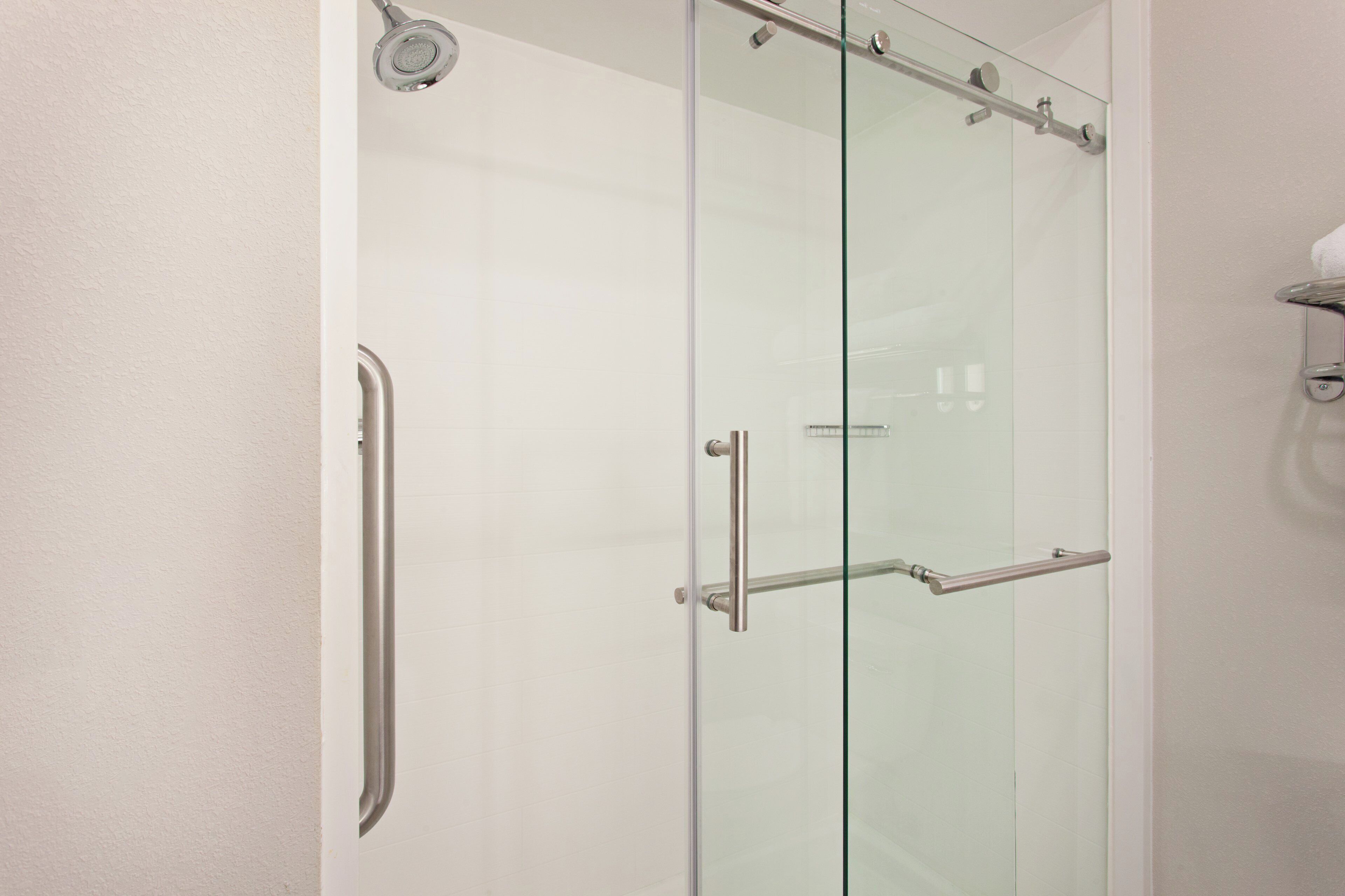 A glass-enclosed shower with a handrail and a towel rack.