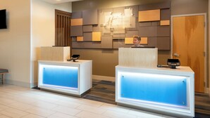 A hotel reception area with two reception desks, a wall-mounted sign, and a wooden door.