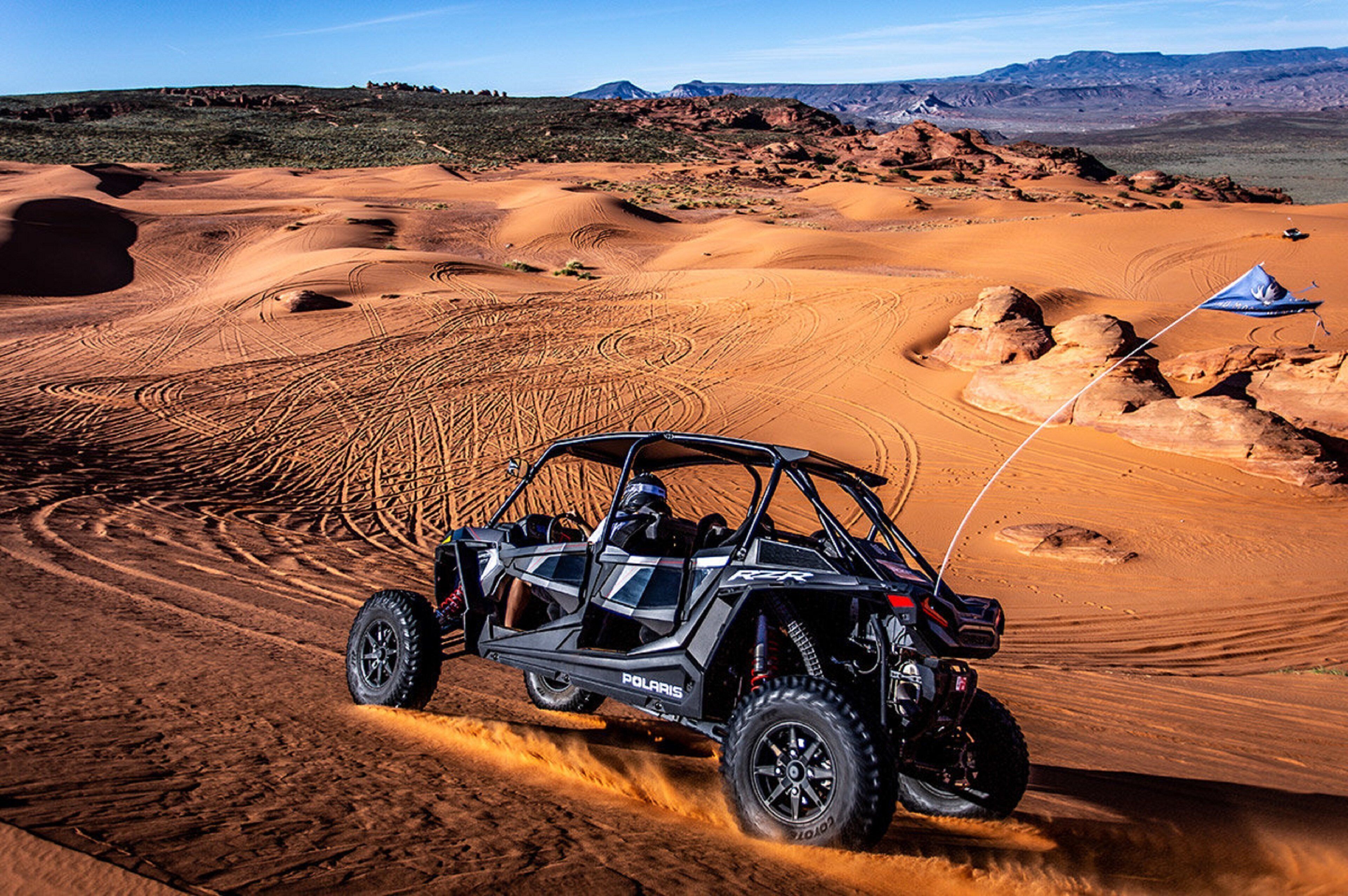 A Polaris RZR off-road vehicle on a sandy terrain with a flag.