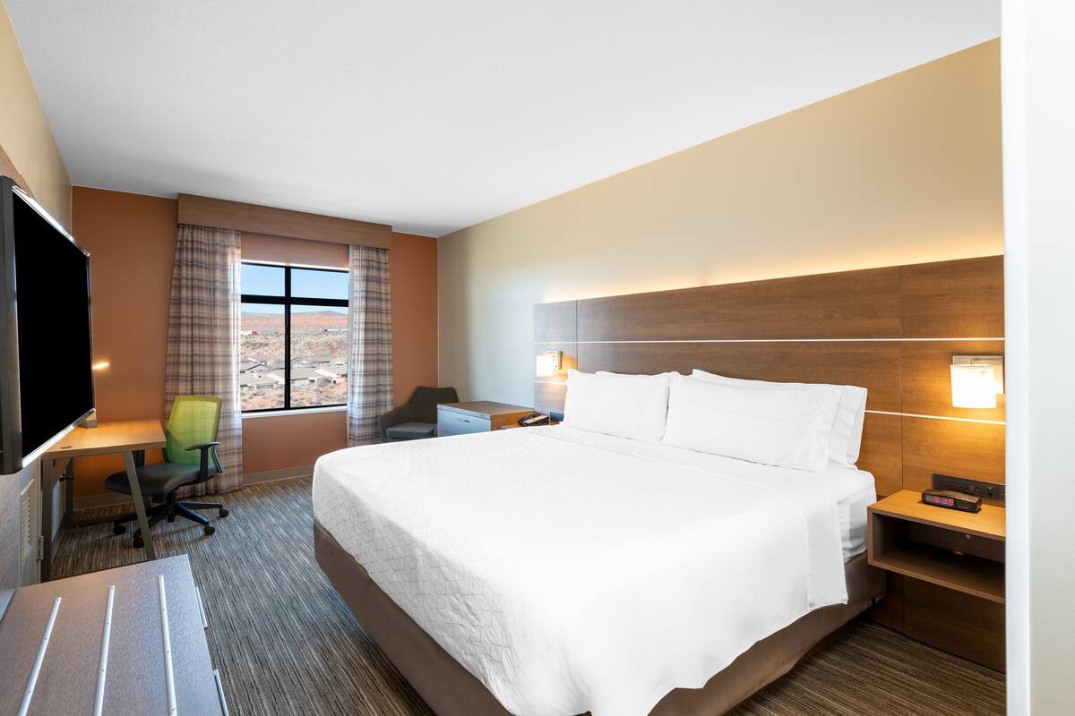 A hotel room with a large bed, a desk with a chair, a TV, and a window with curtains.