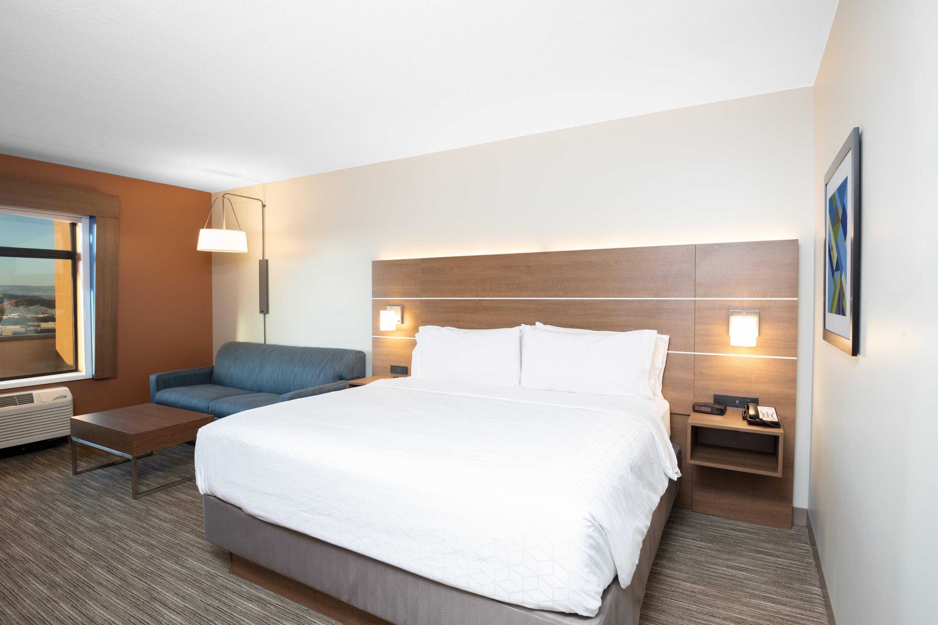 Una habitación de hotel con una cama grande, un sofá, un escritorio y una mesita de noche con lámpara y teléfono.