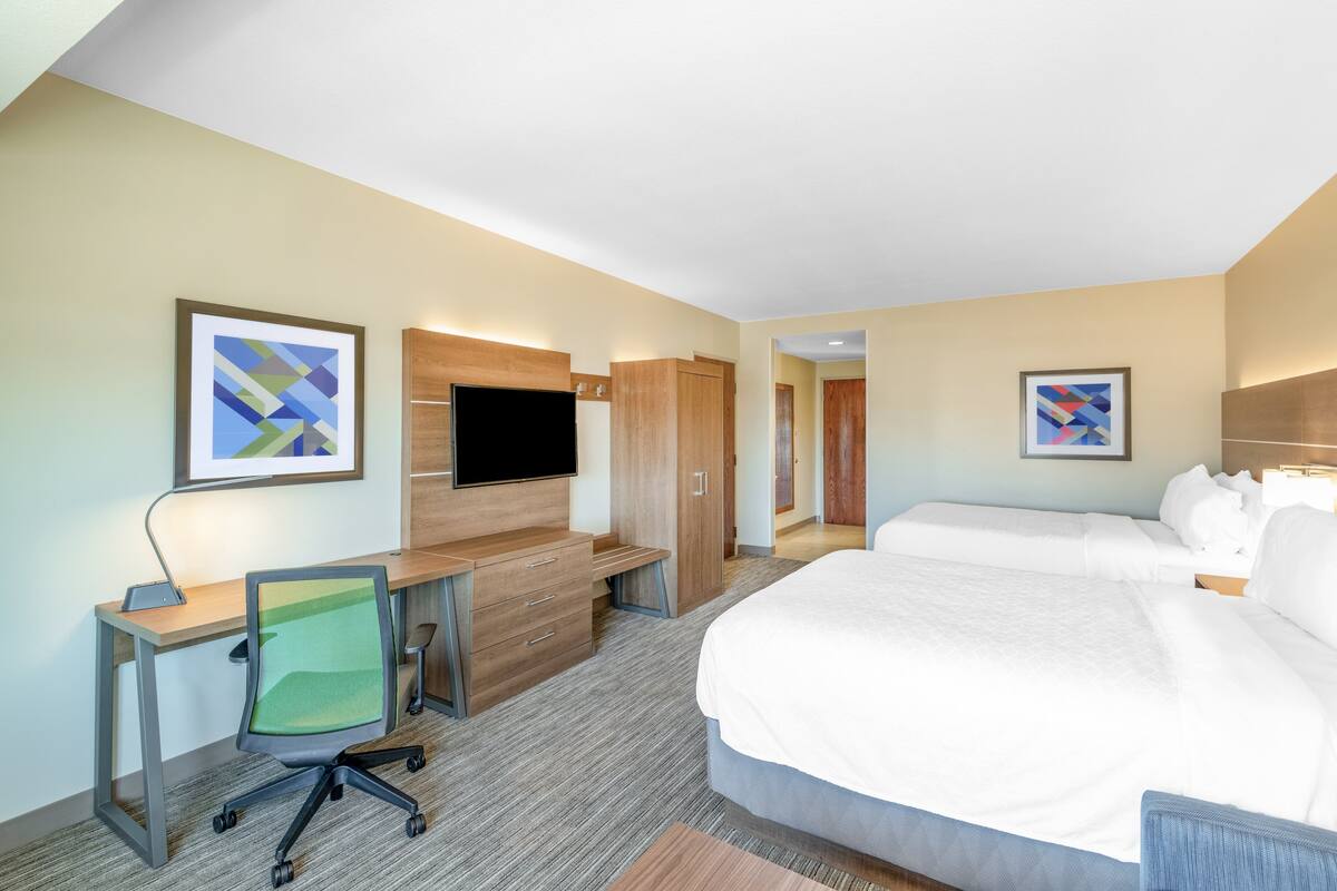 A hotel room with a bed, desk, chair, TV, and artwork on the walls.