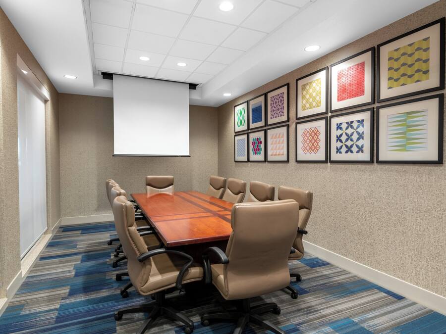 A conference room with a long table, multiple chairs, a projector screen, and patterned wall art.