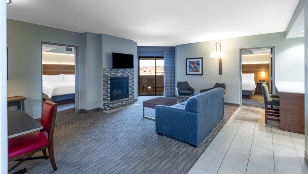 A hotel room with a living area, a fireplace, a sofa, a TV, and a bed. - Holiday Inn Express & Suites St. George North - Zion by IHG (Washington)