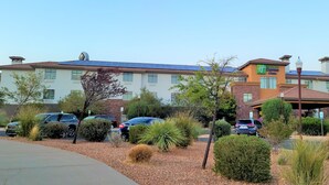 Edificio de Holiday Inn Express con estacionamiento, varios automóviles y un jardín bien cuidado con arbustos y plantas diversas.