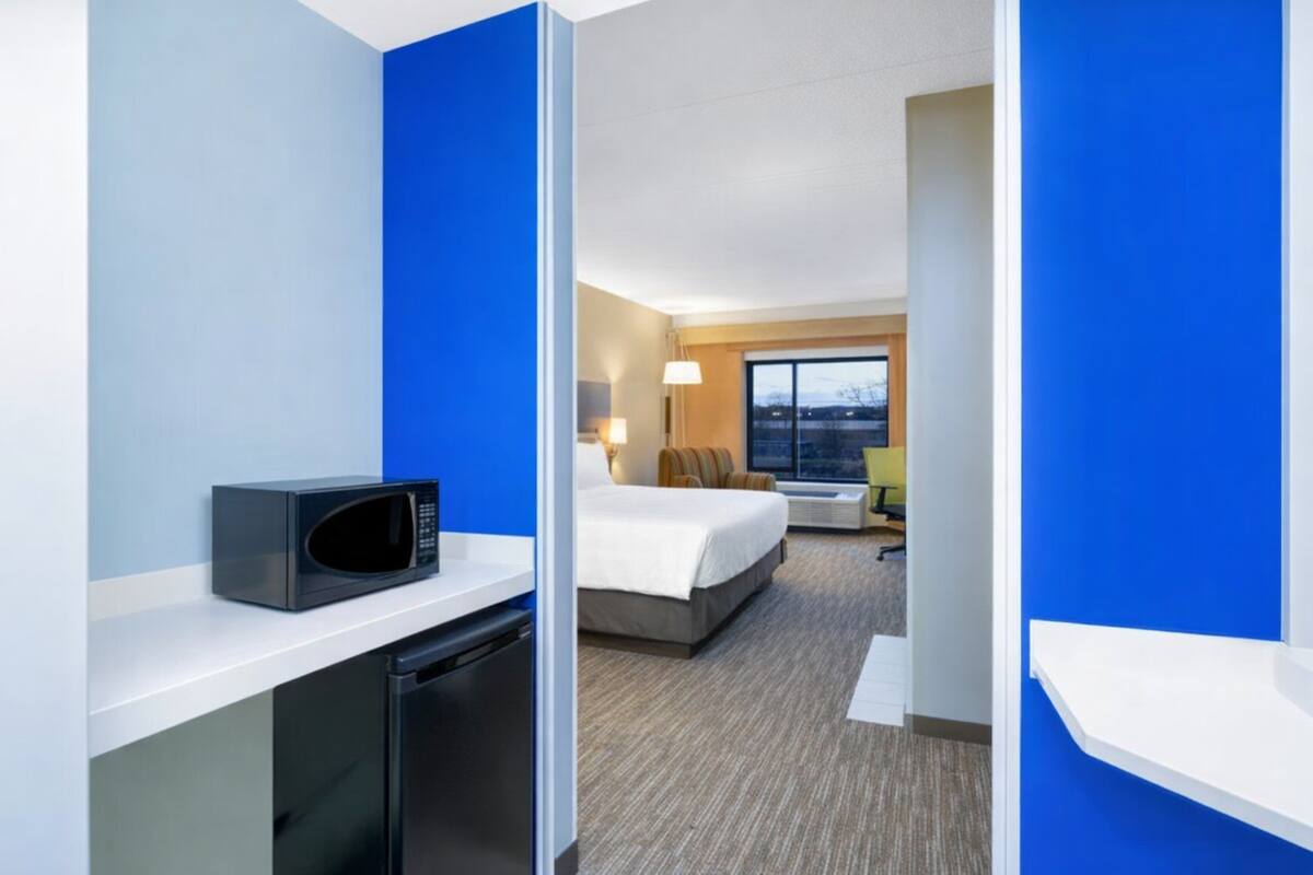 A hotel room with a microwave, a bed, a desk, and a window with a view.
