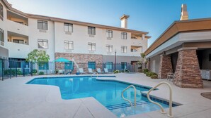 A swimming pool with a stone wall and a building with multiple balconies in the background.