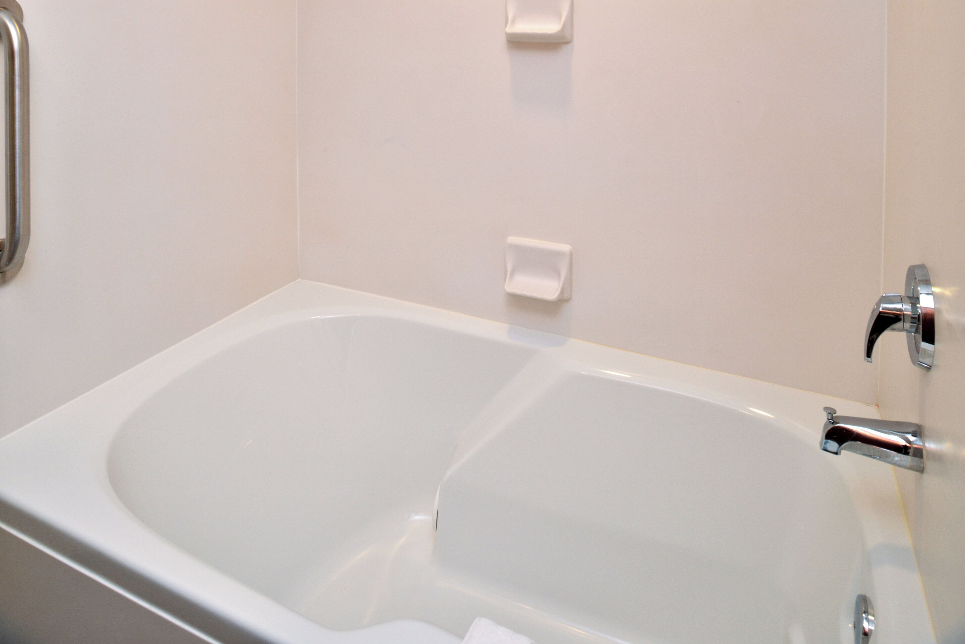 A modern bathroom with a large bathtub, a chrome faucet, and a small white soap dish on the wall.