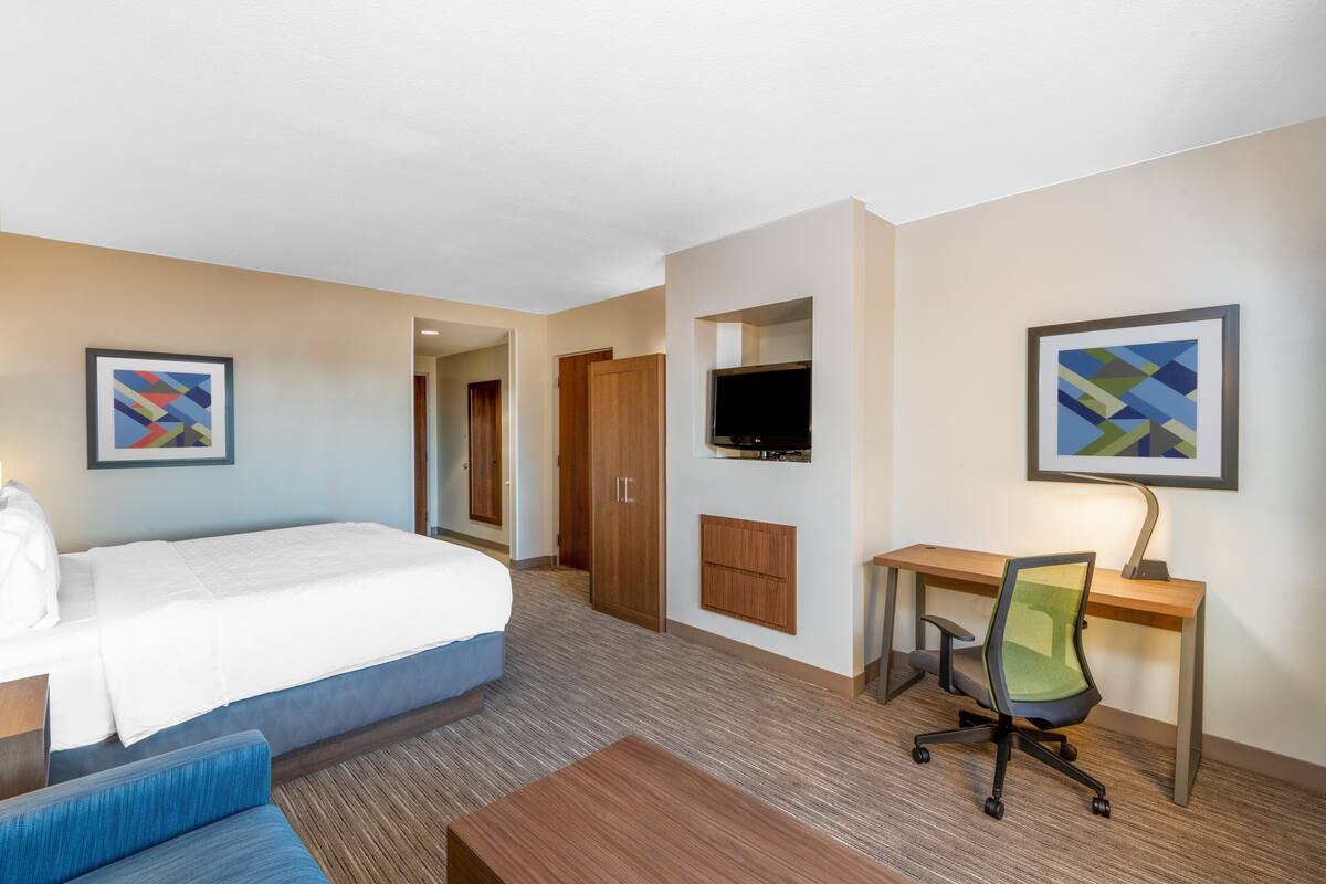 A hotel room with a bed, a desk, a chair, a TV, and artwork on the walls.