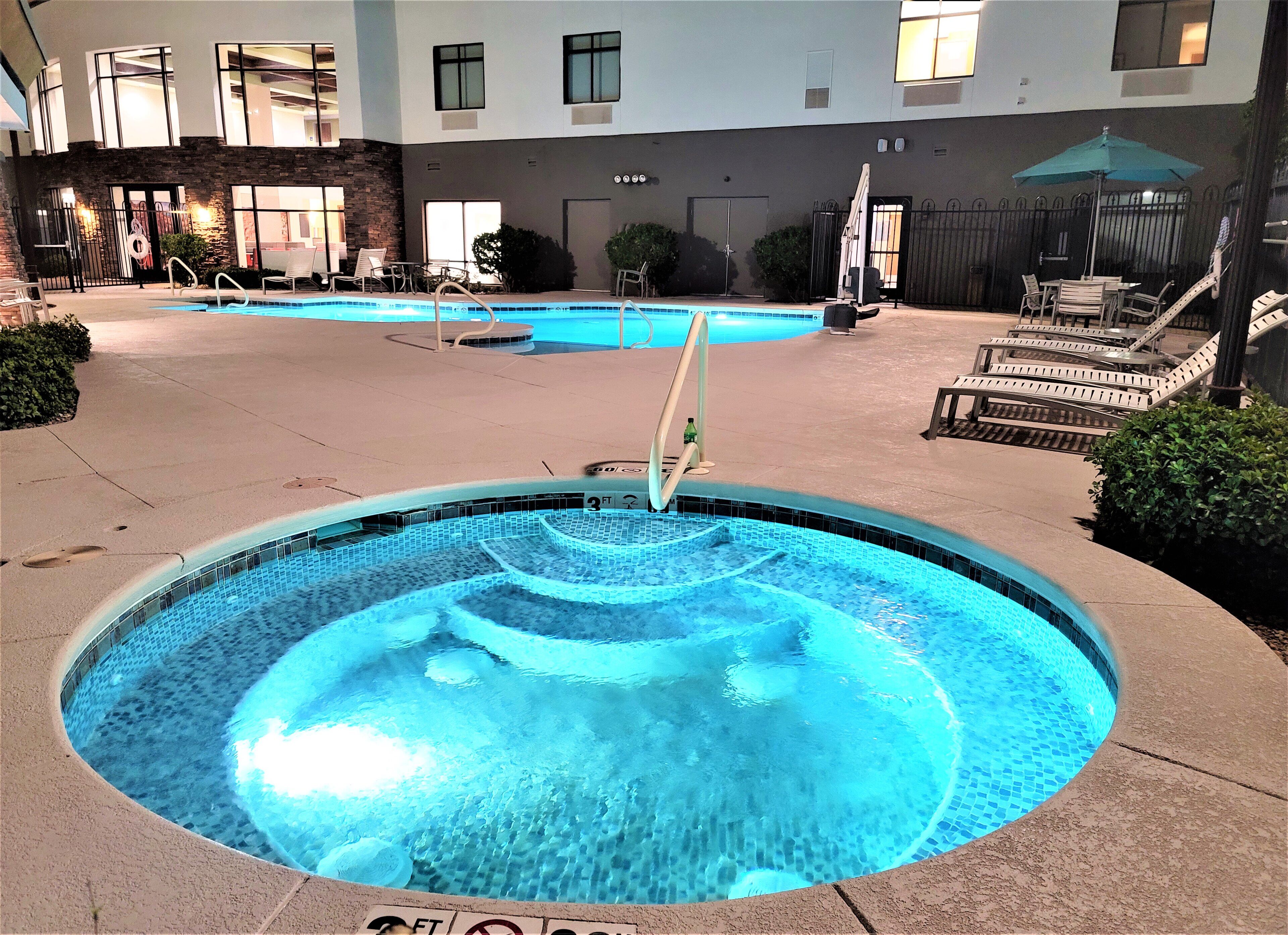 A swimming pool with a water feature, surrounded by lounge chairs and a building in the background.
