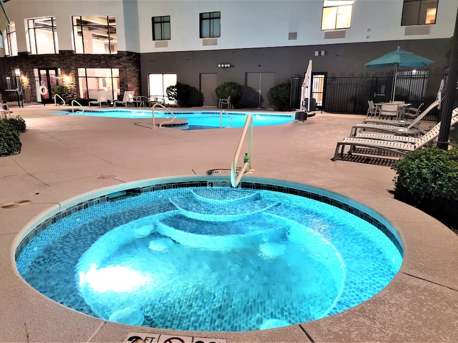 A swimming pool with a water feature, surrounded by lounge chairs and a building in the background.