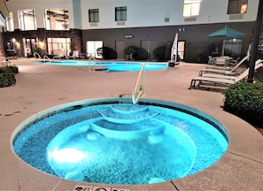A swimming pool with a water feature, surrounded by lounge chairs and a building in the background.