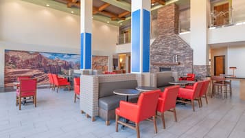 Un vaste espace intérieur doté de hauts plafonds, d’une cheminée en pierre et de plusieurs coins salon, comprenant des chaises rouges et des bancs rembourrés.