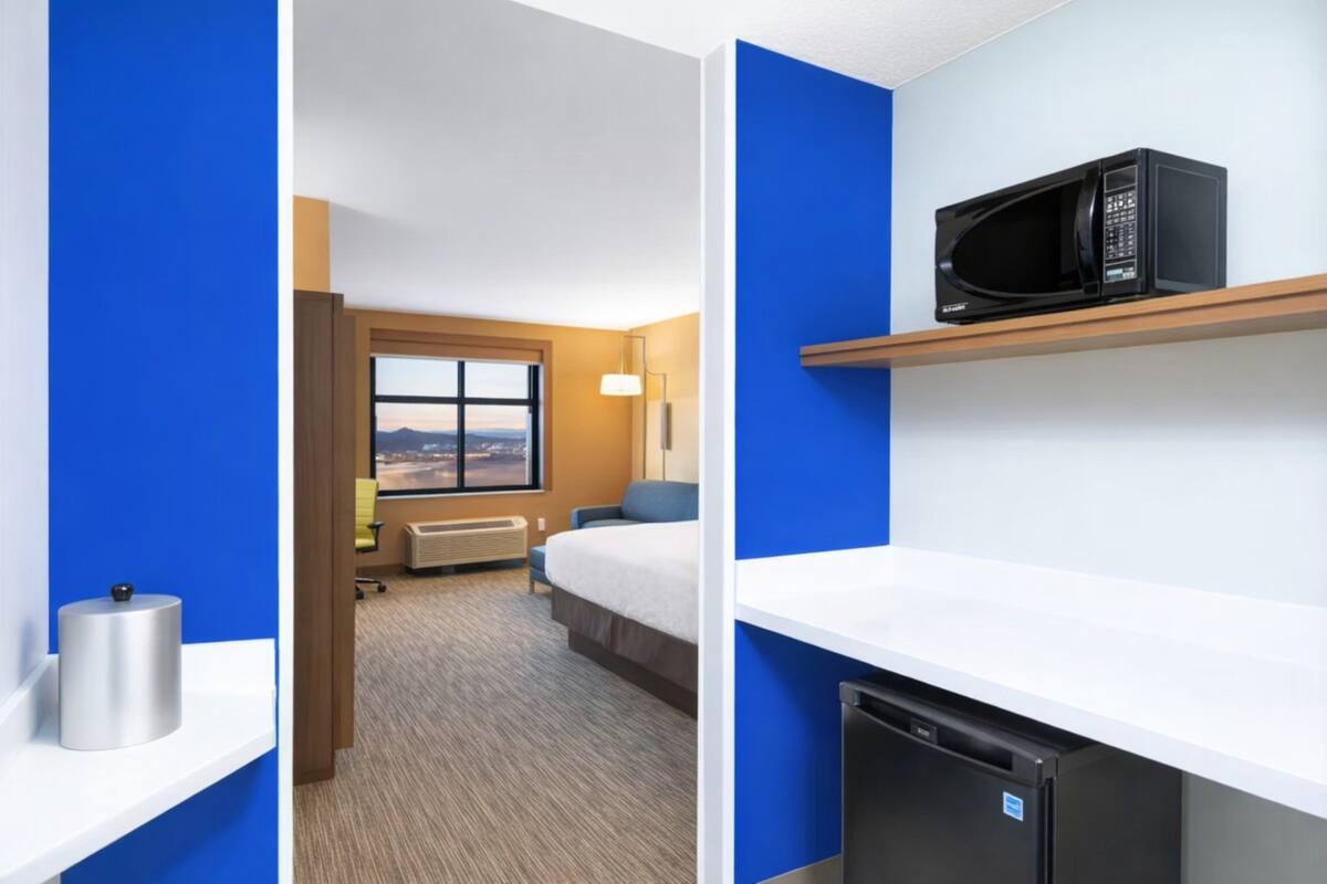A hotel room with a bed, a desk, a microwave, and a small refrigerator.