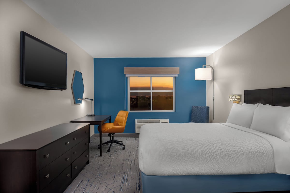 A hotel room with a bed, desk, chair, TV, and a window with a view.