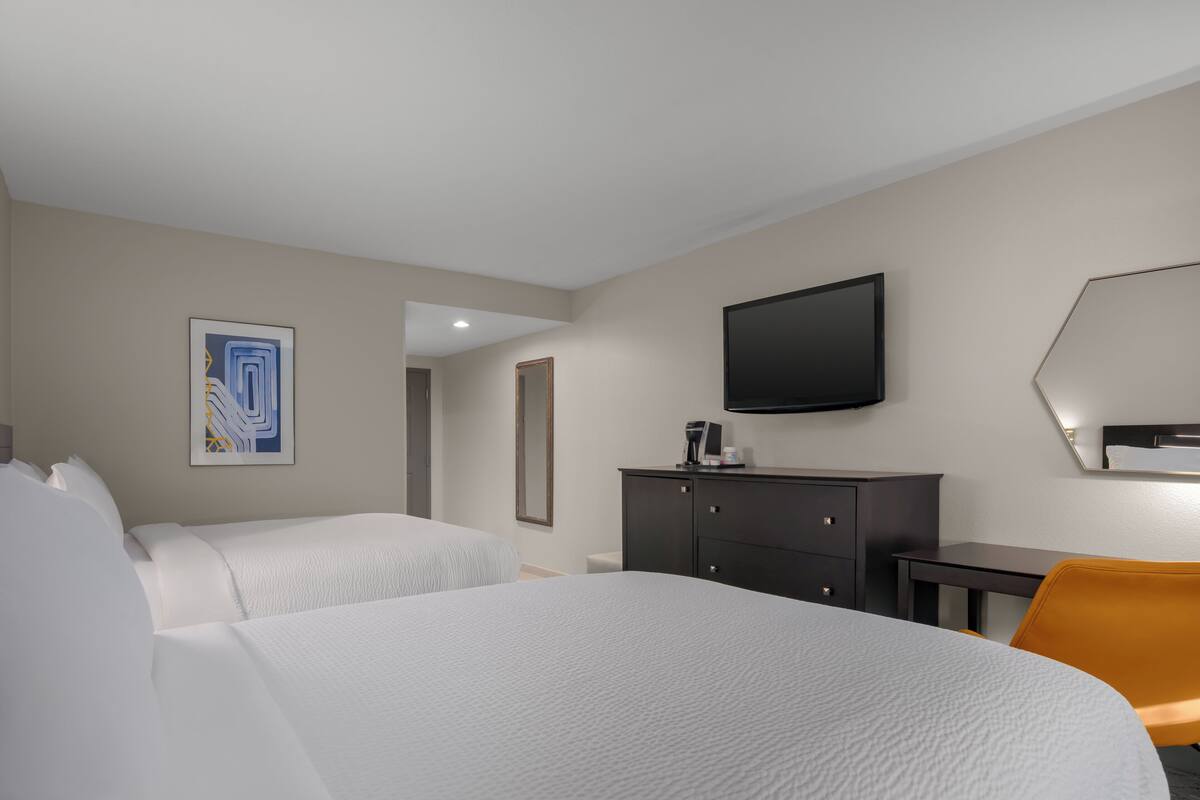 A hotel room with a bed, a desk, a chair, a television, and a painting on the wall.