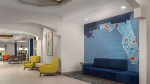 A modern lobby with a blue map mural, yellow and blue seating, and a dining area in the background. - Holiday Inn Express & Suites Kendall by IHG (Miami)