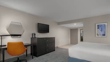 A hotel room with a bed, a desk, an orange office chair, a dresser, a television, and a framed picture on the wall.