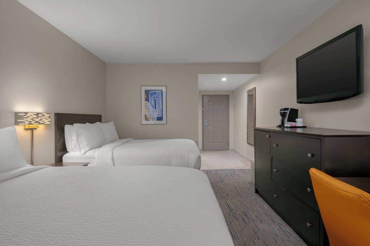 A hotel room with two beds, a desk, a television, and a door leading to another room.