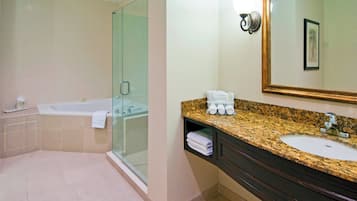 A bathroom with a glass-enclosed shower, a bathtub, a sink with a granite countertop, and a mirror with a framed picture.