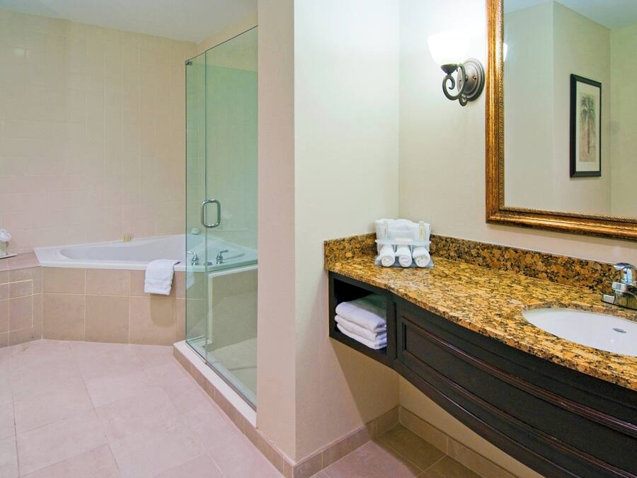 A bathroom with a glass-enclosed shower, a bathtub, a sink with a granite countertop, and a mirror with a framed picture.