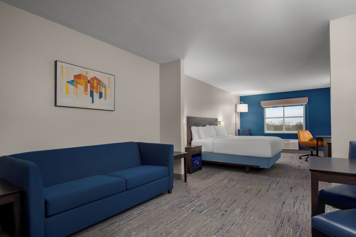Quarto de hotel com um sofá azul, uma cama, uma mesinha e um quadro na parede.