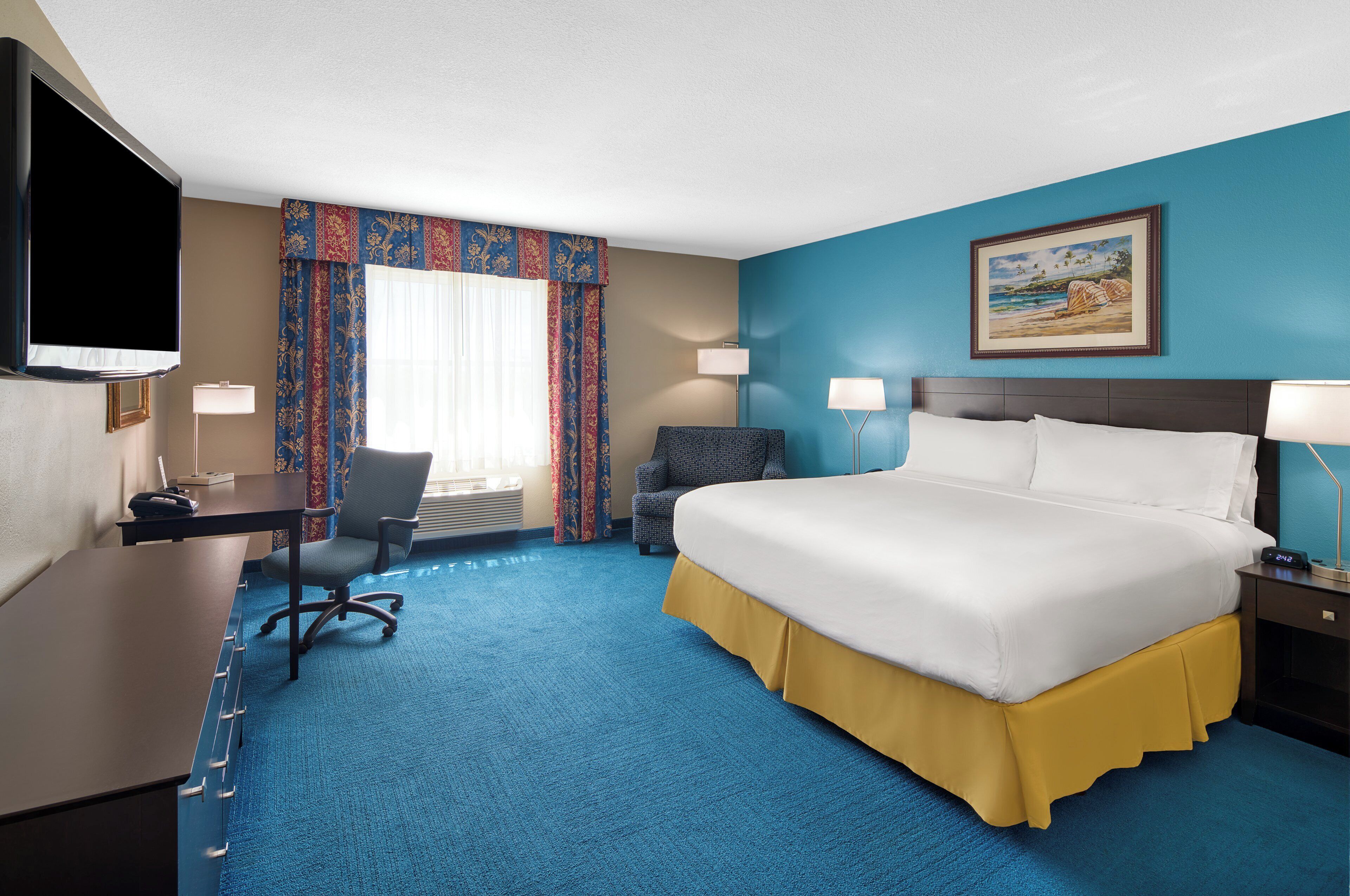 A hotel room with a large bed, a desk, a chair, a TV, and a painting on the wall.