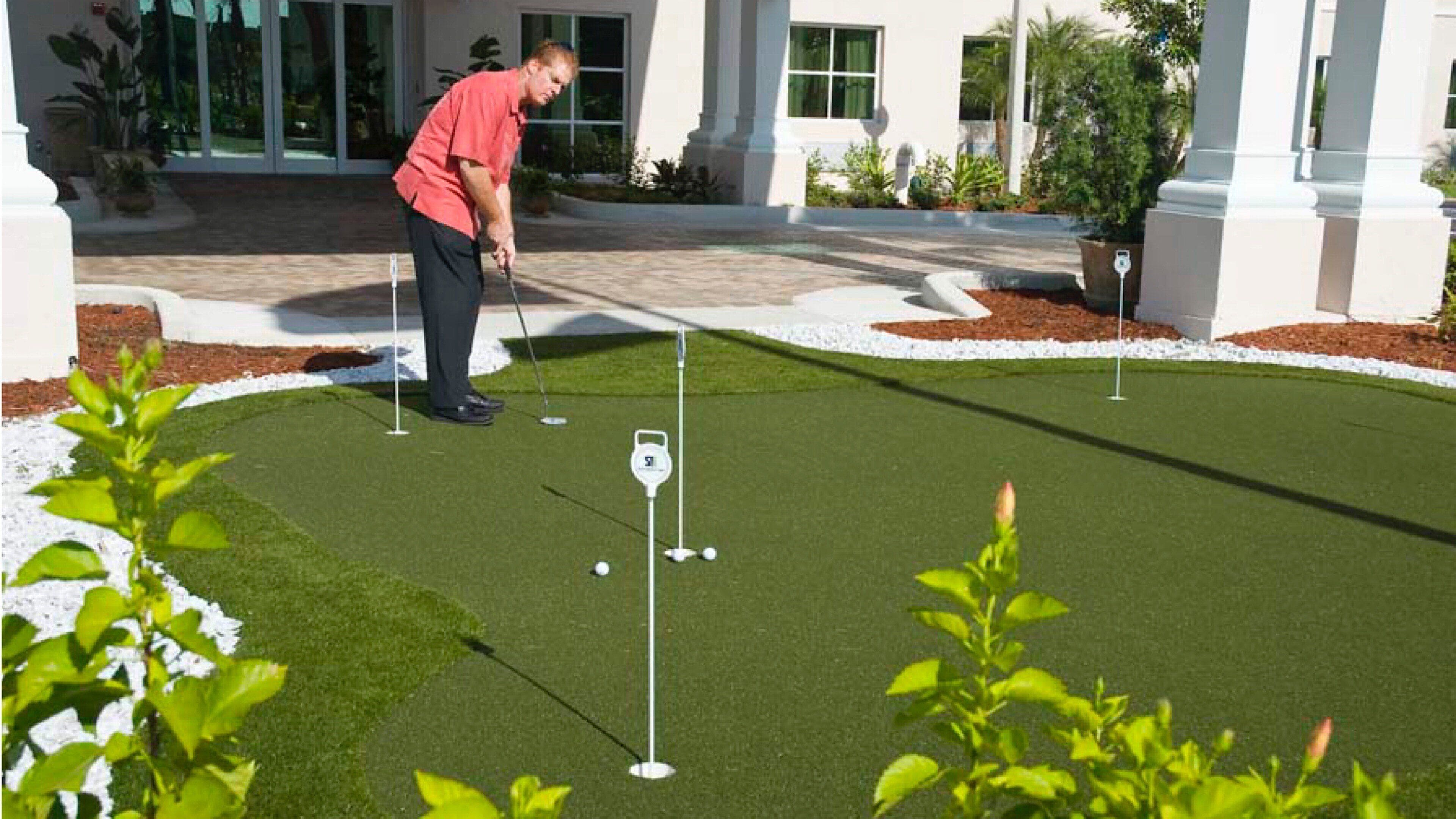 Un campo de golf con un putting green, un palito de bandera y un golfista con una camiseta roja.