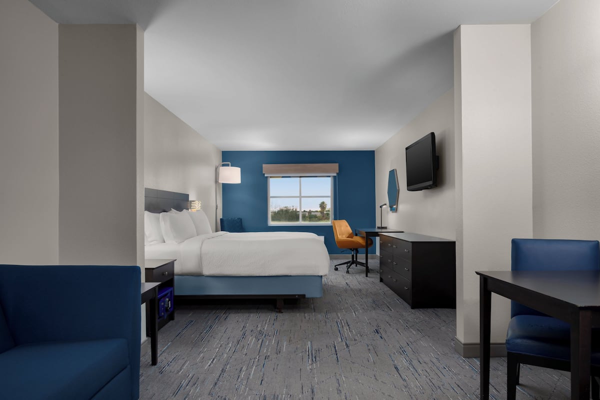 A hotel room with a bed, a desk, a chair, a TV, and a window.