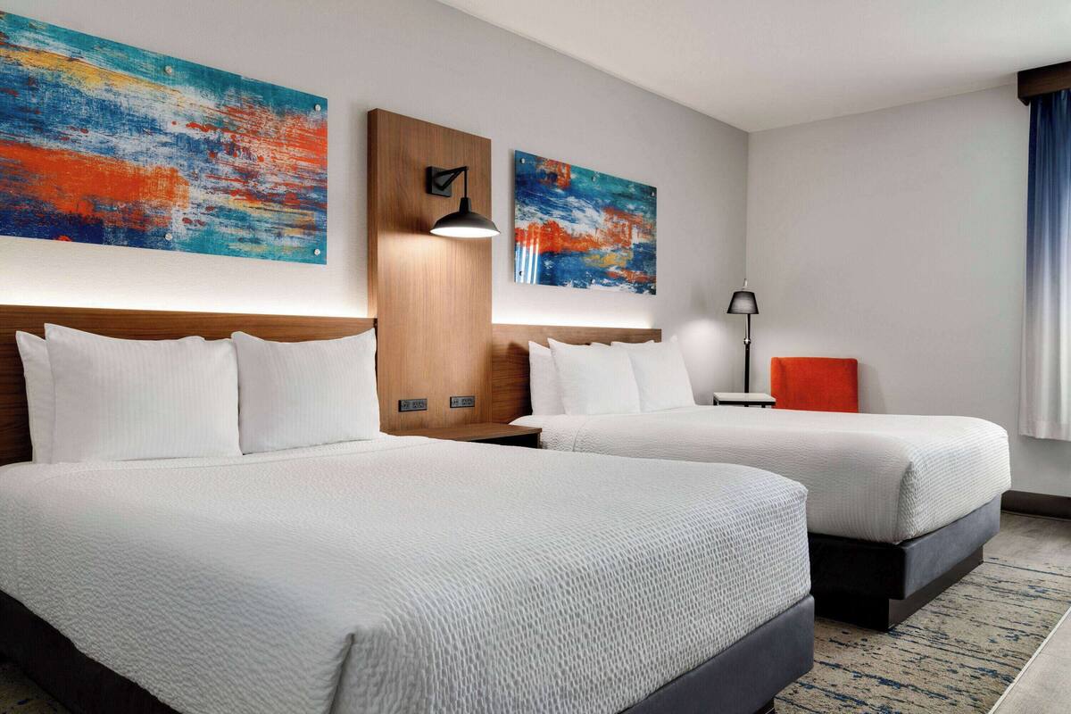 Een hotelkamer met twee bedden, een houten hoofdeinde, een nachtkastje, een lamp en twee abstracte schilderijen aan de muur.