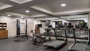 Un gimnasio con cintas de correr, elípticas y una banca para pesas.
