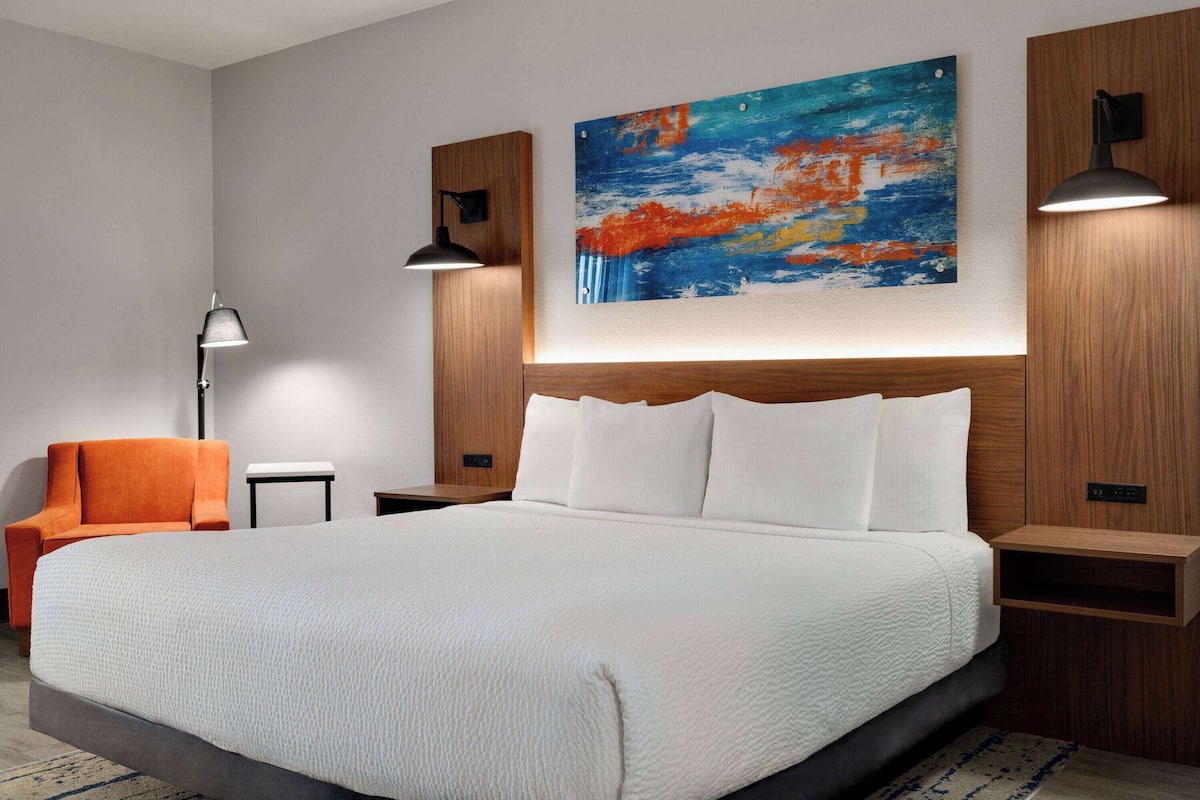 Een moderne hotelkamer met een groot bed, een oranje fauteuil, een tafeltje en een schilderij aan de muur.