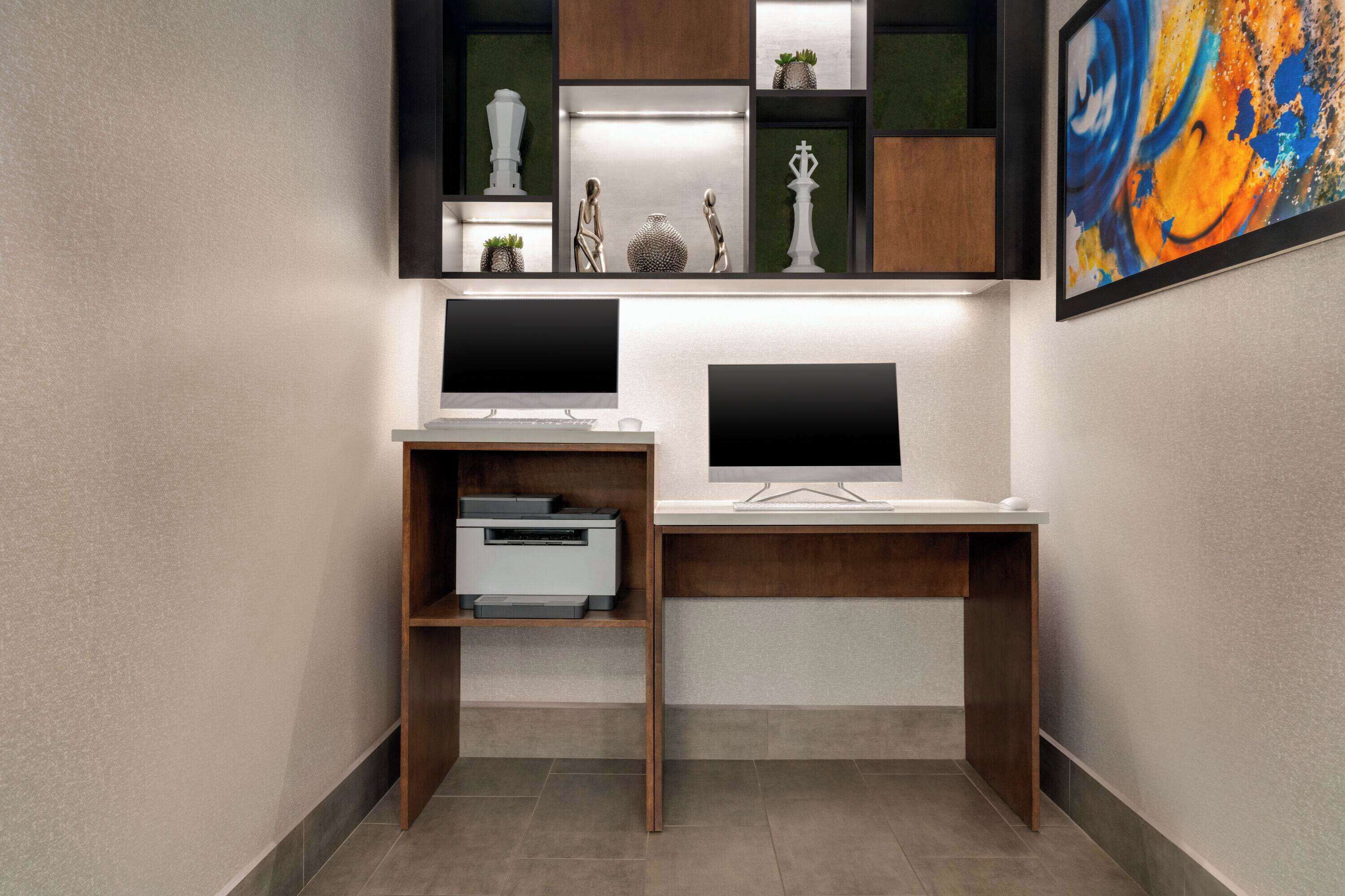 A modern office space with two desks, each with a computer monitor, printer, and decorative items.