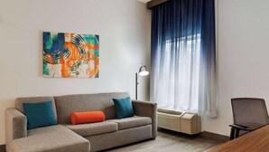 Una sala de estar moderna con un sofá seccional gris, un escritorio y un cuadro abstracto grande en la pared.