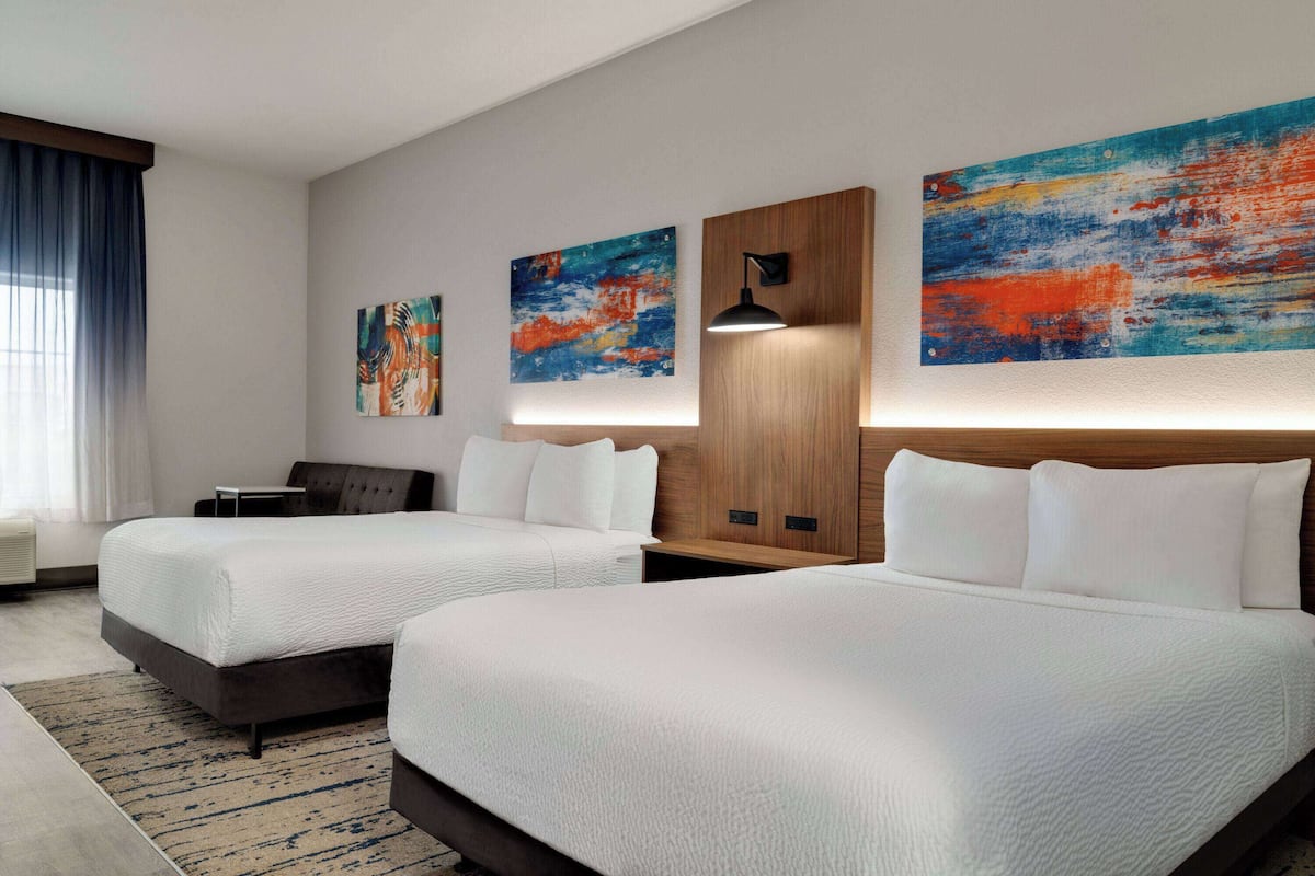 Een hotelkamer met twee bedden, een houten hoofdeinde, een wandlamp en abstracte schilderijen.