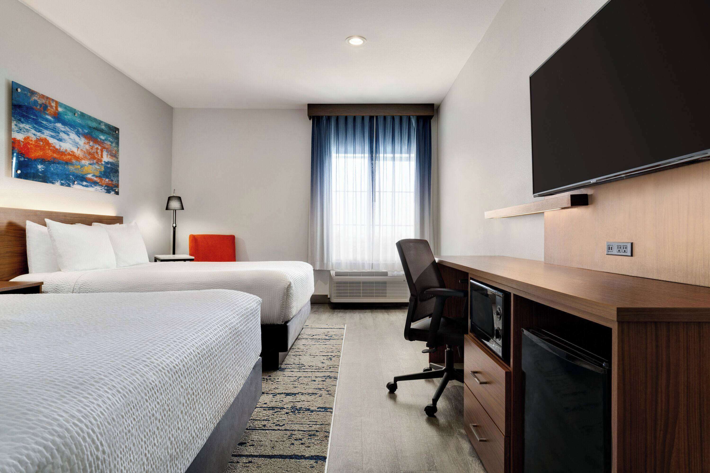 Een hotelkamer met twee bedden, een bureau, een flatscreen televisie en een groot raam met gordijnen.