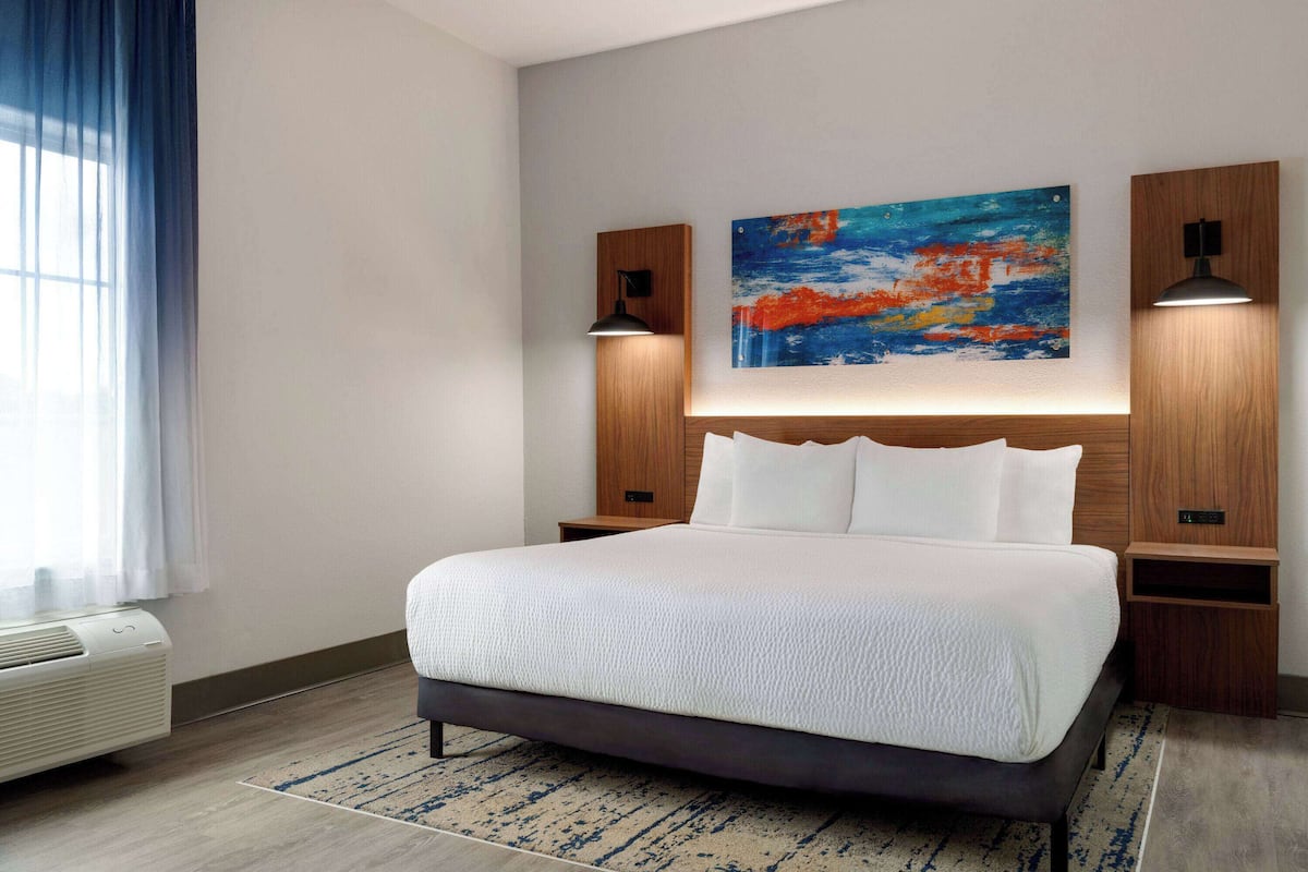 Een moderne hotelkamer met een groot bed, een schilderij aan de muur en twee bedlampjes.
