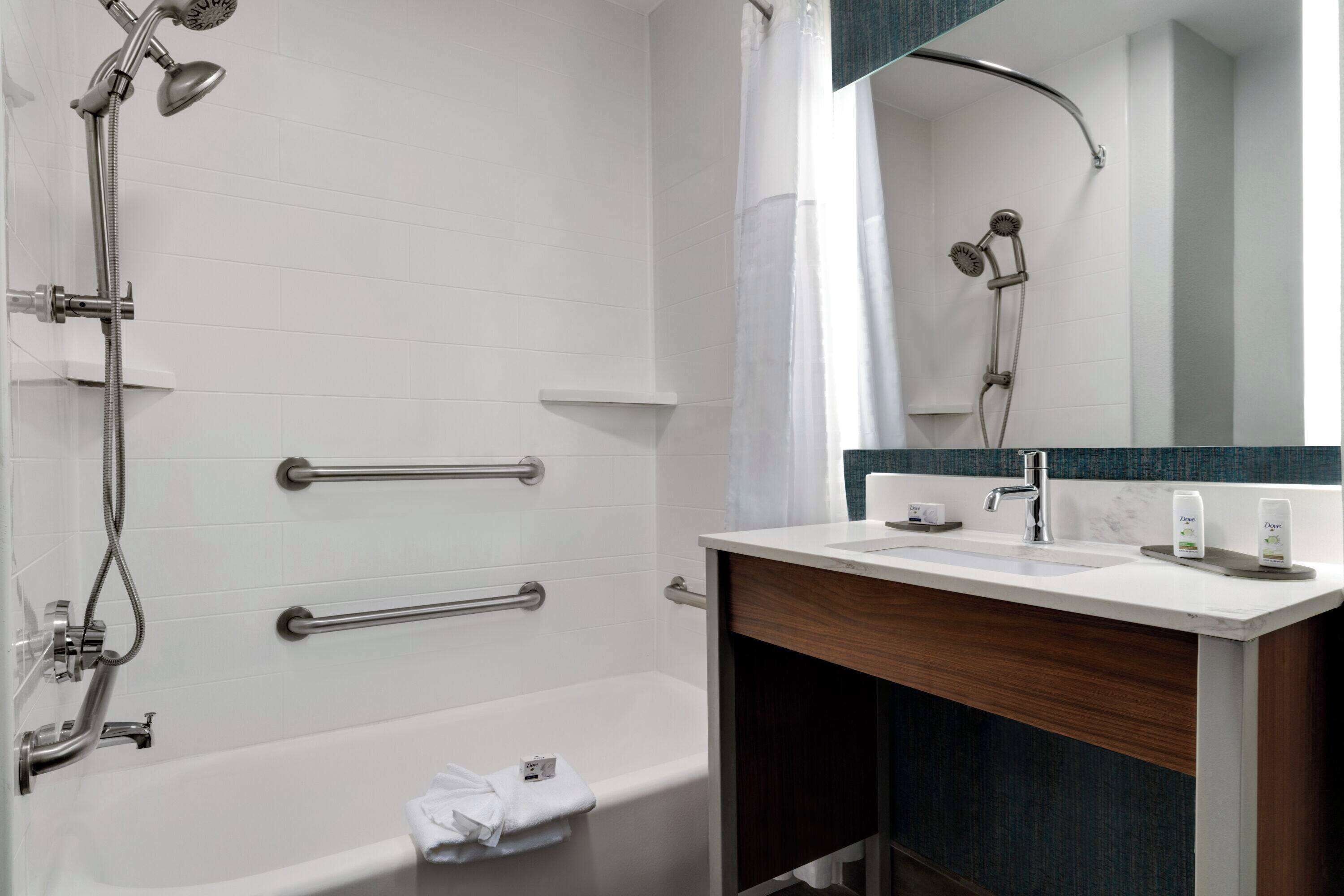 Een moderne badkamer met een bad, een douche met handdouche, een wastafelmeubel en een spiegel.