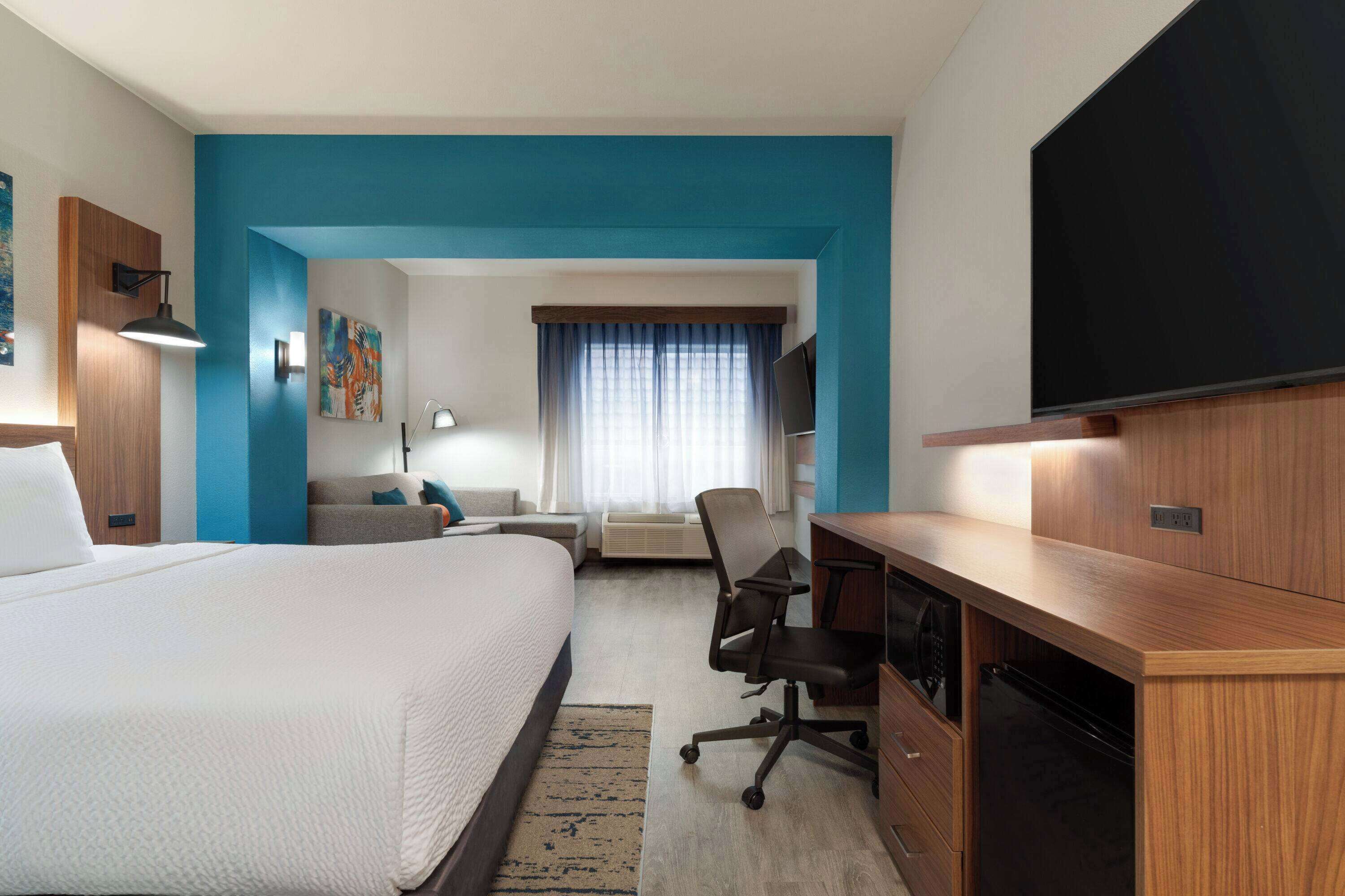 A modern hotel room with a large bed, a desk, a chair, a television, and a window with curtains.