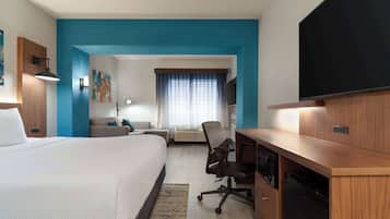 Una habitación de hotel moderna con una cama grande, un escritorio, una silla, un televisor y una ventana con cortinas.