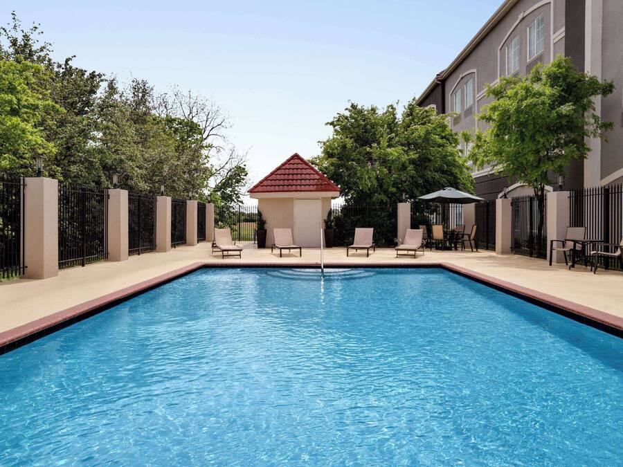 A rectangular swimming pool with a tiled deck, surrounded by a fence and trees.