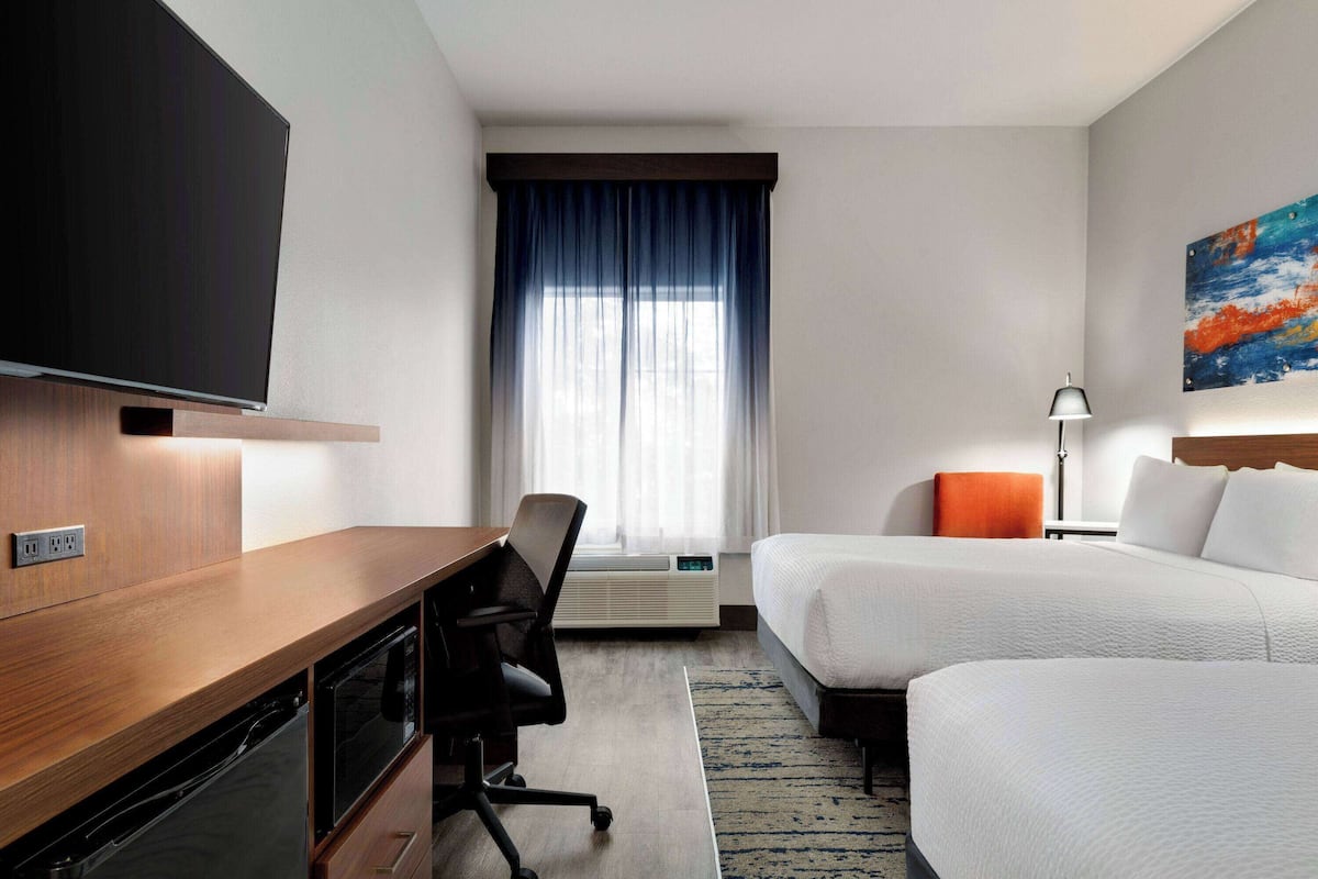 Hotelkamer met een houten bureau, een flatscreen televisie, twee bedden, een bureaulamp en een schilderij aan de muur.