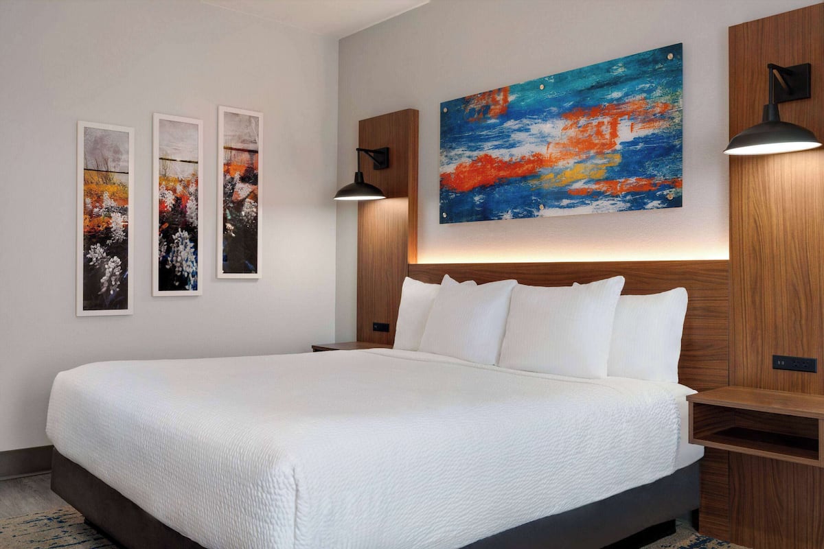 Een moderne slaapkamer met een groot bed, een houten hoofdeinde en drie ingelijste kunstwerken aan de muur.