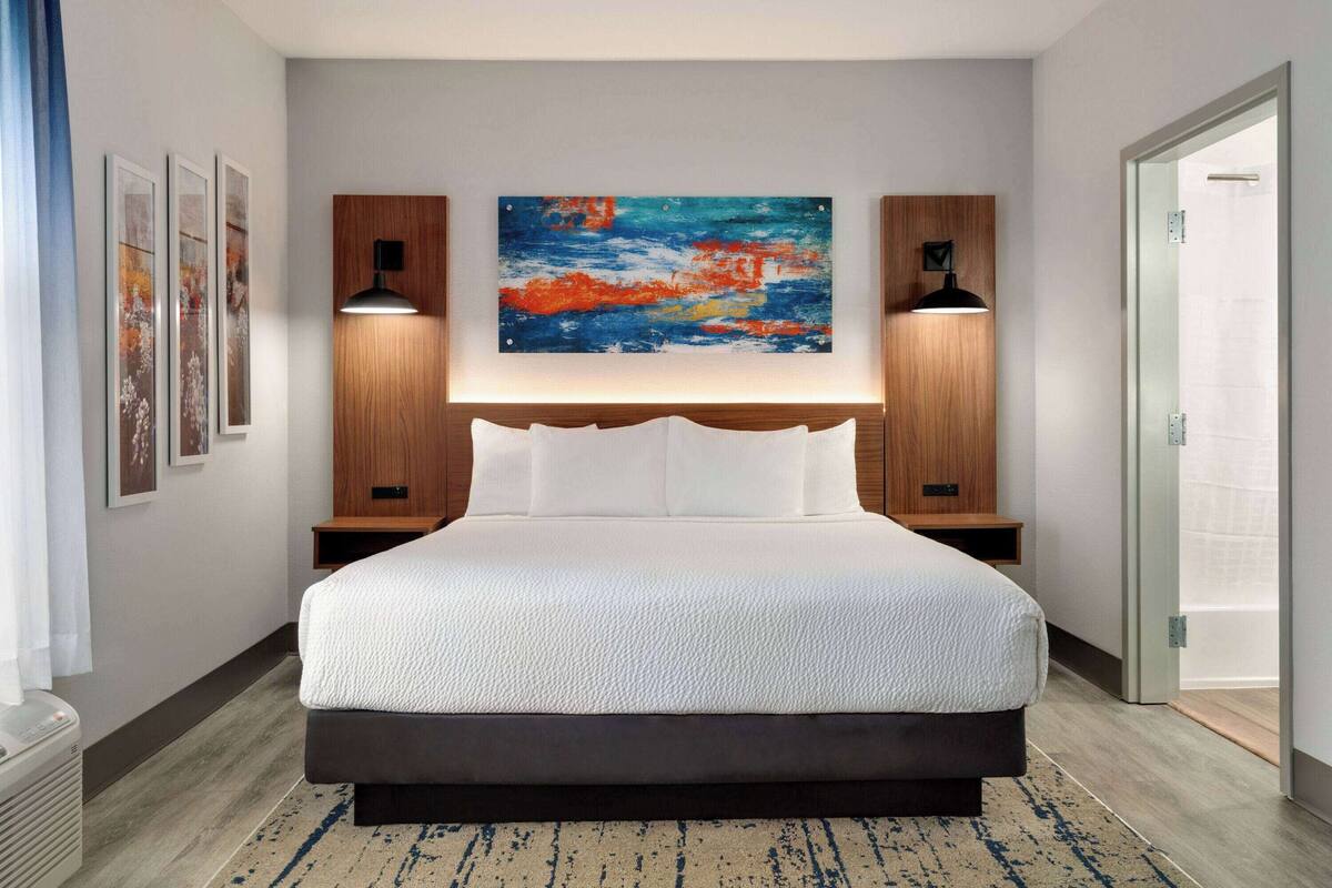 Een moderne hotelkamer met een groot bed, een schilderij aan de muur en een houten hoofdeinde.