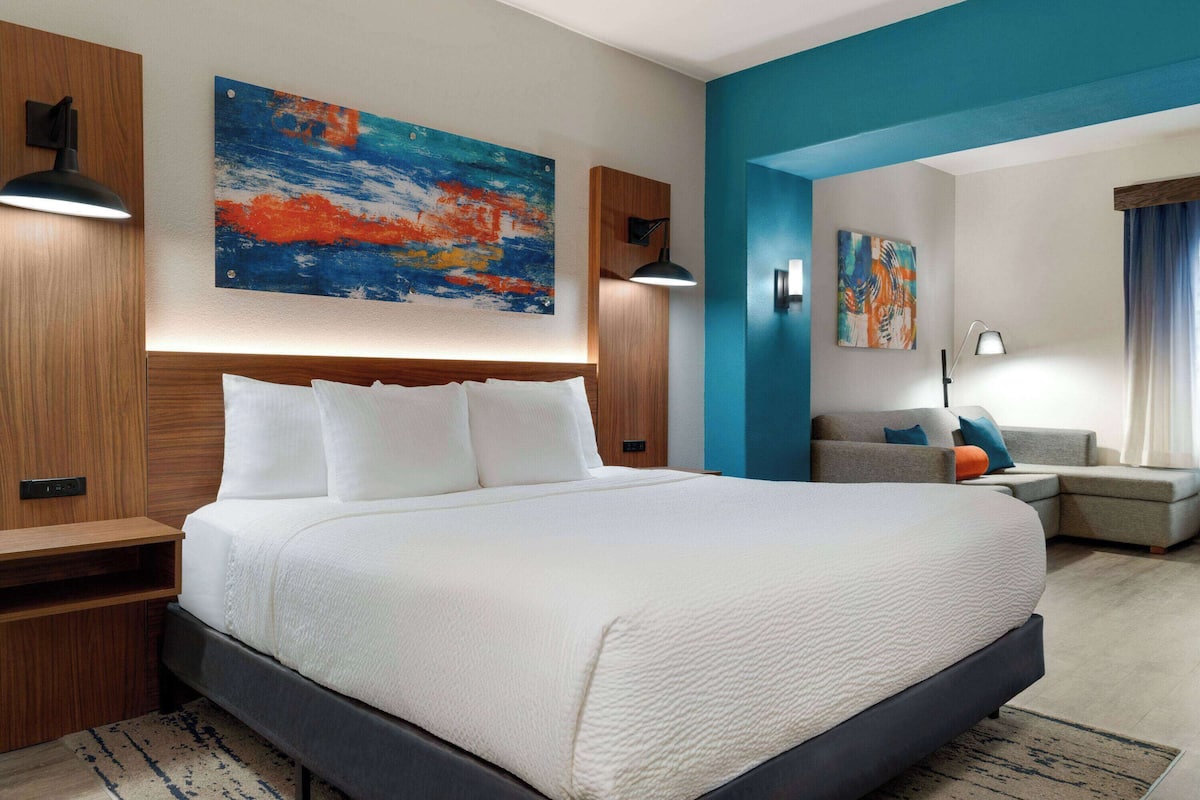 Een moderne hotelkamer met een groot bed, een houten hoofdeinde en een blauwe accentmuur.
