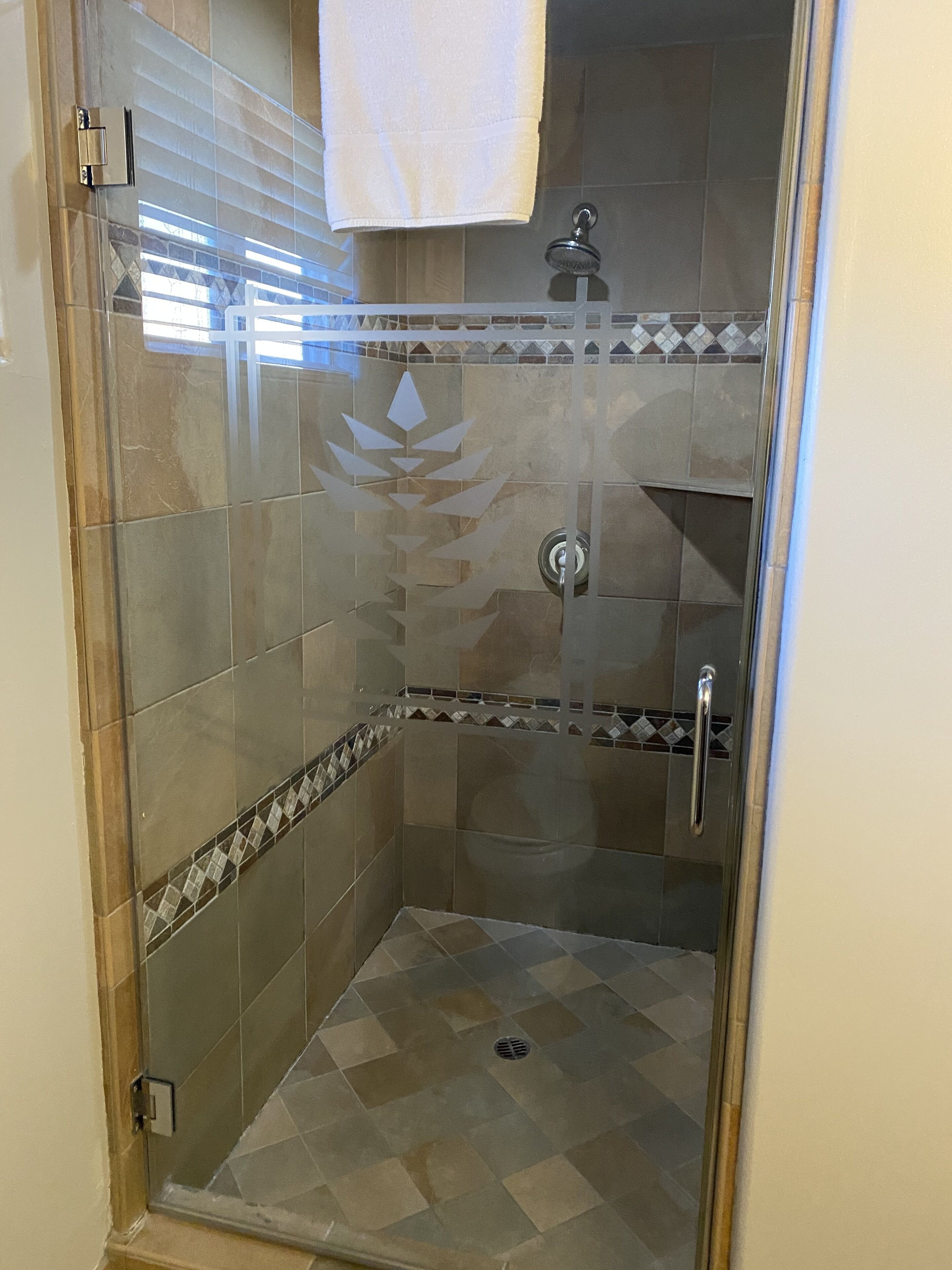 Una ducha con cerramiento de vidrio, piso de baldosas y una banda decorativa de azulejos.